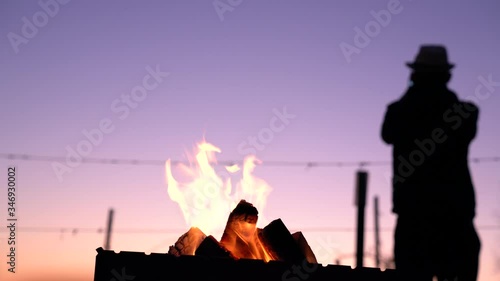 Silhouette of a man who stands back to the camera and recording video of a beautiful colorful sunset on the phine, a fire burns in the grill photo