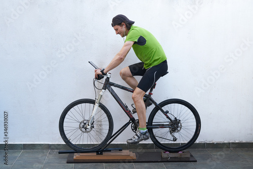 green t-shirt cyclist riding an exercise bike with a homemade roller, looking at the tablet