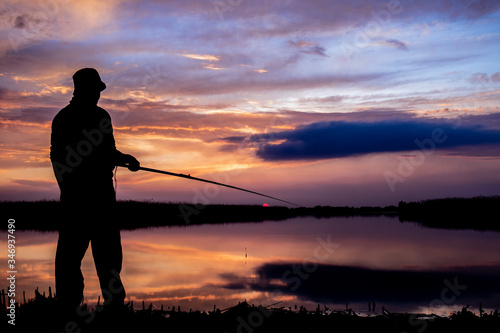 Fisher man fishing on a lake bank at sunset