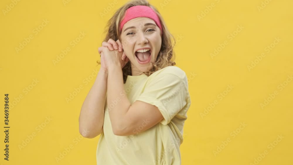 A happy young athletic woman in sportswear is rejoicing isolated over a yellow background in studio