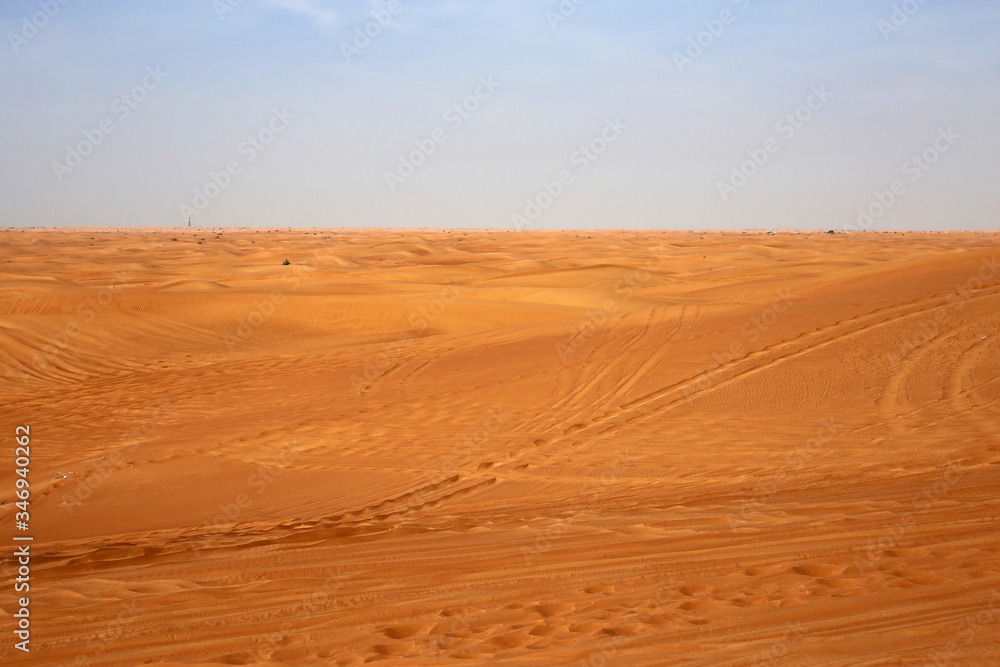 Red sand dunes in Sharjah, UEA during a sunny day. A lot of sand and plenty of tire marks and some footprints since there has been tourists doing dune bashing, walking and enjoying the Middle East.