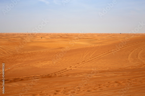 Red sand dunes in Sharjah, UEA during a sunny day. A lot of sand and plenty of tire marks and some footprints since there has been tourists doing dune bashing, walking and enjoying the Middle East.