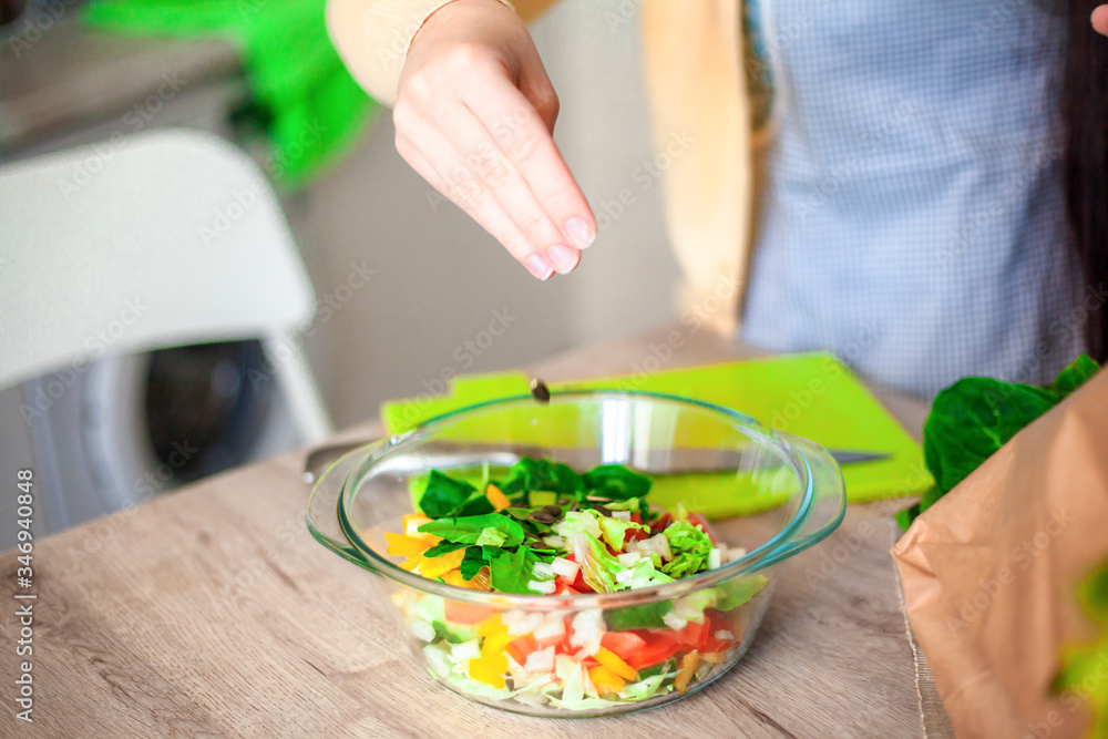 Young brunette woman making healthy food on the dinner table in the kitchen. Female cooking fresh vegan salad with green vegatable Young brunette woman making healthy food on the dinner table in the kitchen. Female cooking fresh vegan salad with green vegatable