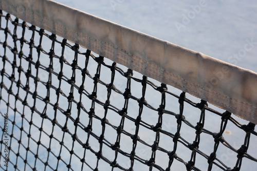 Tennis court net in a closeup. Tennis is a fun leisure activity during summer and springtime and suits well to healthy and active lifestyle. Tennis is also a great vacation sport. Closeup color photo.
