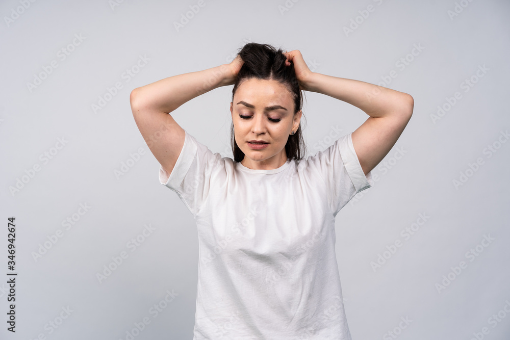 Young girl in white shirt on gray background, hands up in the air and to collect hair, eyes closed, daydreaming Young girl in white shirt on gray background, hands up in the air and to collect hair, eyes closed, daydreaming