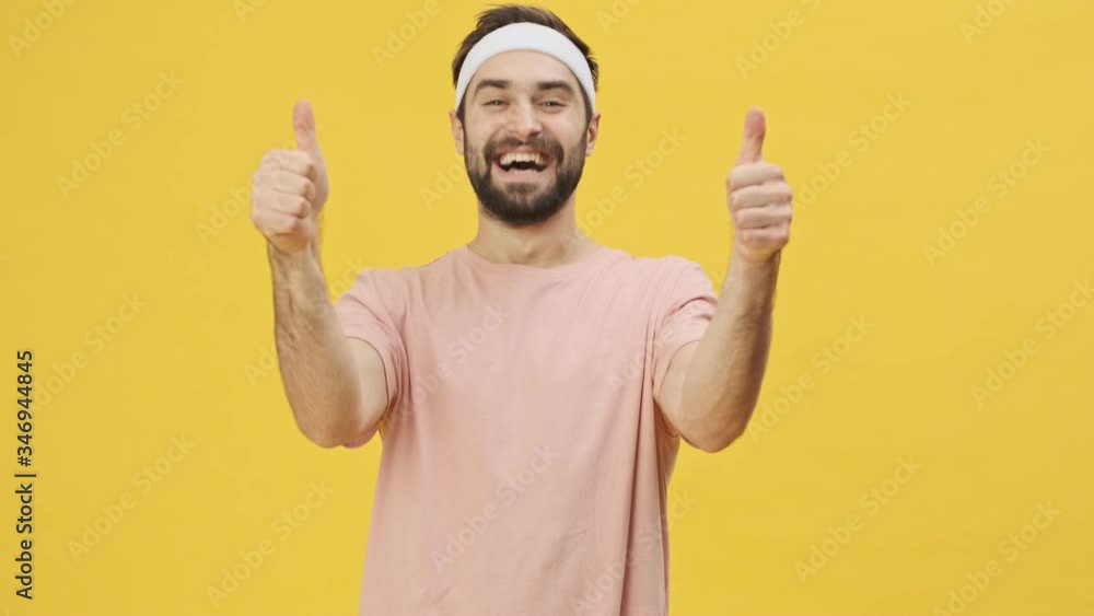 A happy positive young athletic man in sportswear is showing thumb up gesture with both hands isolated over a yellow background in studio A happy positive young athletic man in sportswear is showing thumb up gesture with both hands isolated over a yellow background in studio