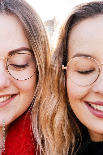 Vertical portrait of couple of blonde sisters with trendy glasses. Close up of young women faces together wearing fashionable frame sight glasses. Optician and sight concept.