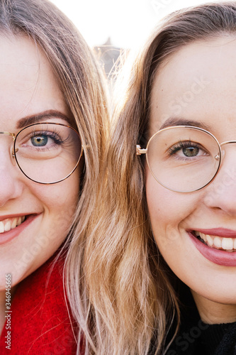 Vertical portrait of couple of blonde sisters with trendy glasses. Close up of young women faces with eyes wide open wearing fashionable frame sight glasses. Optician and sight concept.