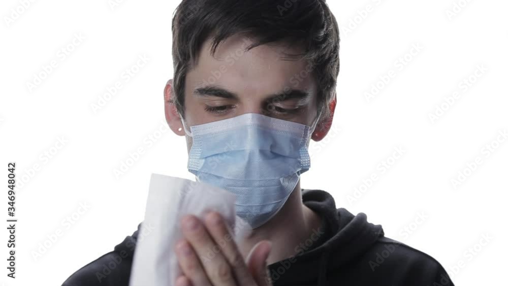 Portrait of a young man in a medical mask who wipes his hands with an antibacterial napkin on white background Portrait of a young man in a medical mask who wipes his hands with an antibacterial napkin on white background