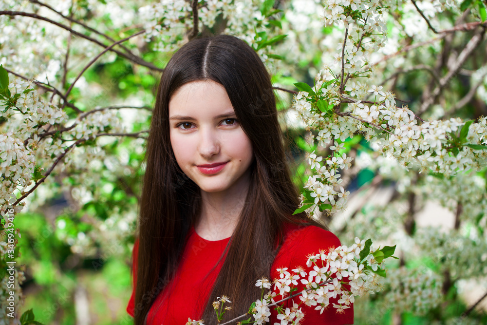 Pretty teen girl are posing in garden near blossom cherry tree with white flowers Pretty teen girl are posing in garden near blossom cherry tree with white flowers