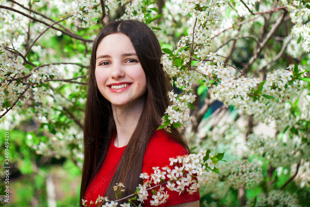 Pretty teen girl are posing in garden near blossom cherry tree with white flowers Pretty teen girl are posing in garden near blossom cherry tree with white flowers