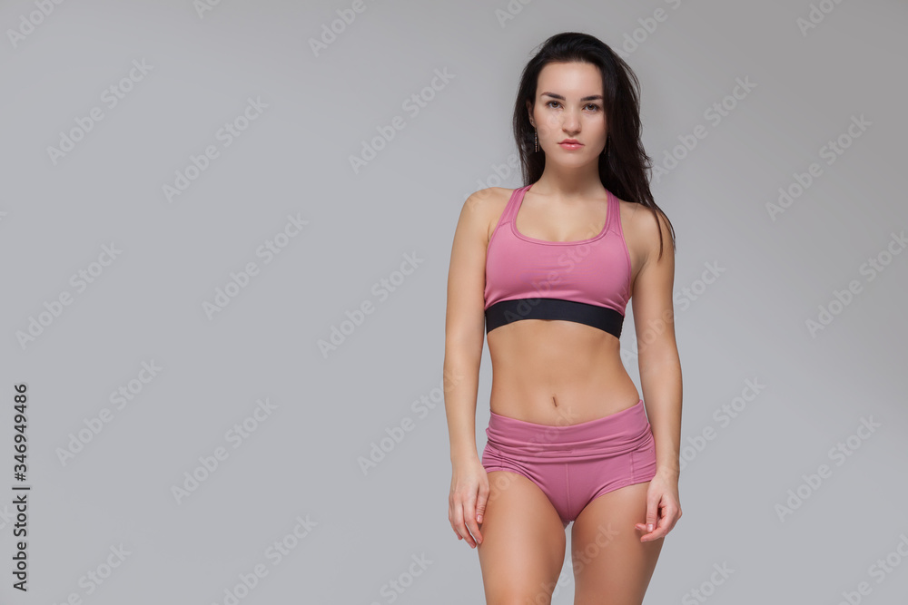 Fototapeta premium Attractive young brunette woman in pink sportswear is posing isolated on grey background