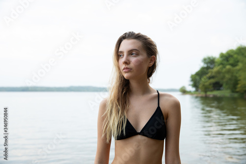 Young female wearing a bikini, lake in the background, looking away.