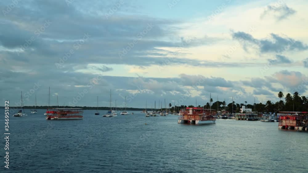 A dock of sail boats and tourist boats on a large river at Alligator beach near Joao Pessoa, Brazil during dusk A dock of sail boats and tourist boats on a large river at Alligator beach near Joao Pessoa, Brazil during dusk