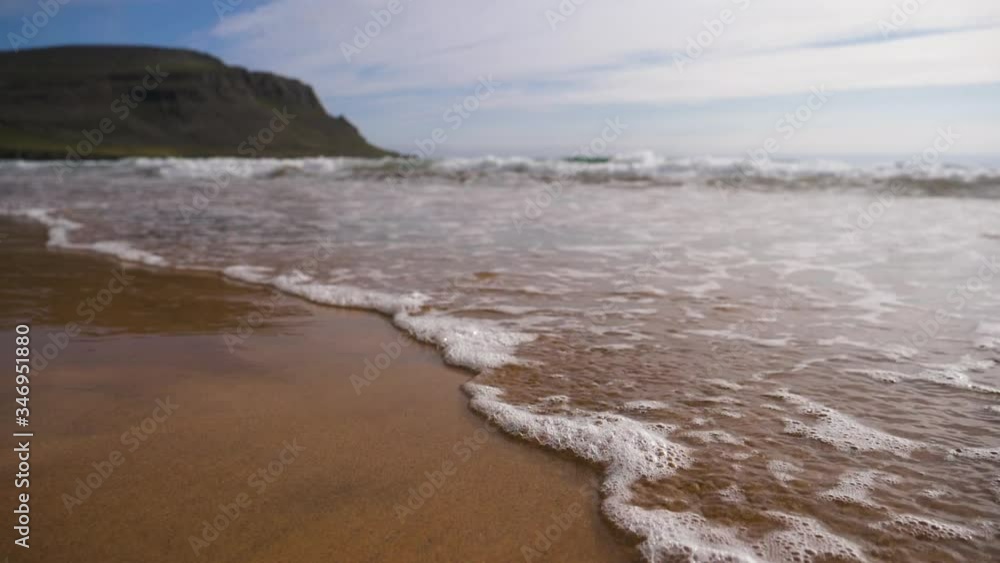 Following waves crashing a beach in Iceland, partly, sunny day - Low, slow motion shot