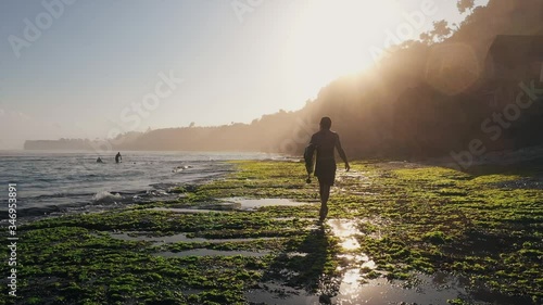 Surfer walking down the reef at sunrise in Bali 