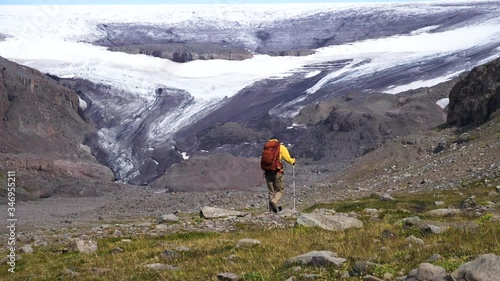 Hiker with hiking poles, walking in rocky nature, towards the Drangajokull glacier, cloudy day. in Iceland photo