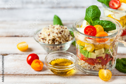 Concept of healthy food, clean eating, low calories delicious meal. Salad with quinoa and fresh vegetables with olive oil in glass jar. Zero waste. Close up wooden background. Copy space