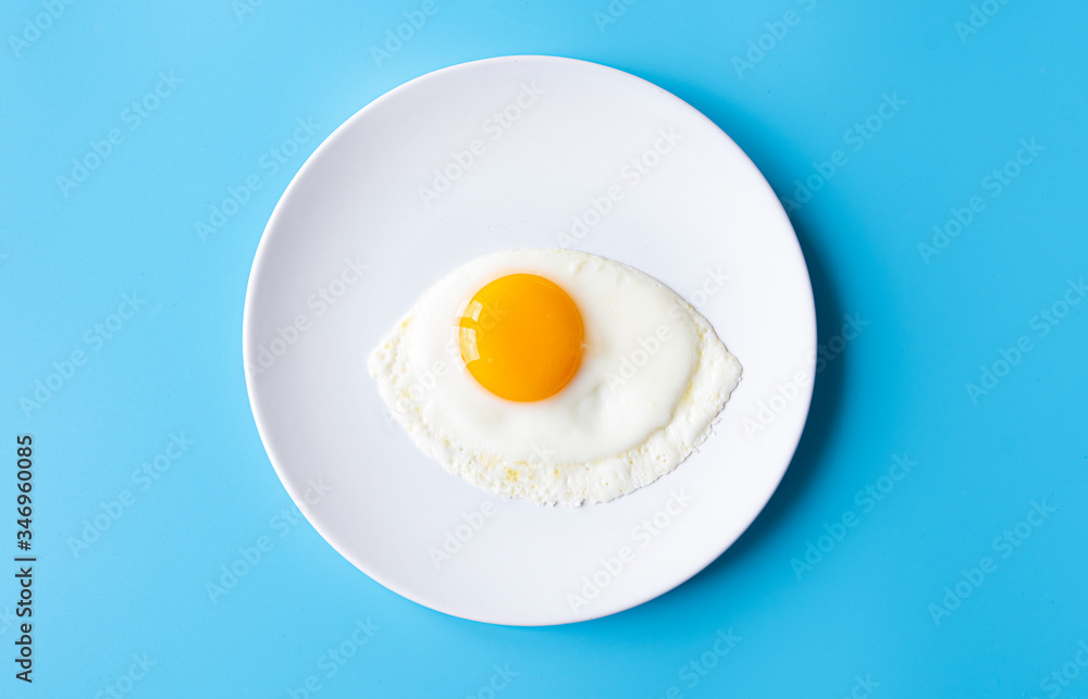 Breakfast, fried egg, yolk, omelet on white plate with color table, creative picture