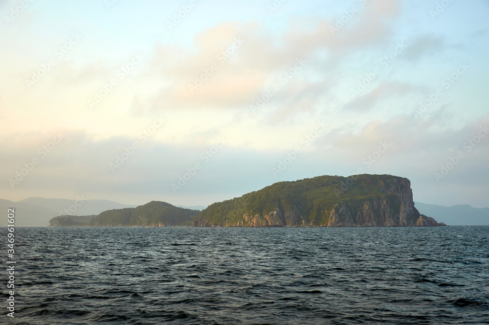 Island in the sea. Island with steep shores in the sea at sunset.