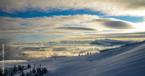 Aerial view above the clouds at mountain peaks covered with snow  lighting by the sun
