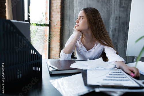 Woman looks thoughtfully out the window during a working day and thinks about future of her company and business due to the economic crisis.