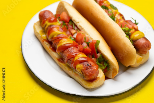 Hot dog with pico de gallo salad on yellow background