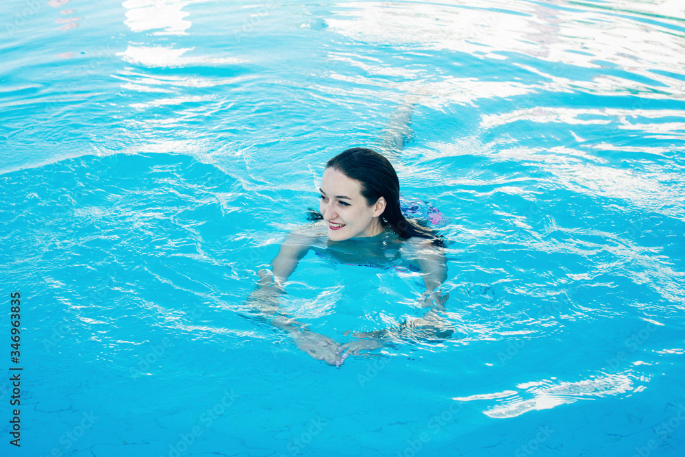 A smiling girl in a blue swimsuit is swimming on the swimming pool. Egypt tour. The morning of a summer day. Luxury vacation. Pleasure, relaxation. Resort. Tourism.