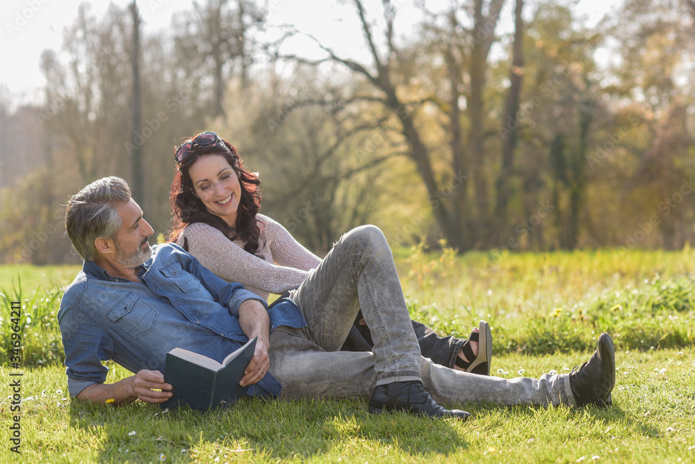 Happy couple reading a book together laying on the grass outdoors Happy couple reading a book together laying on the grass outdoors