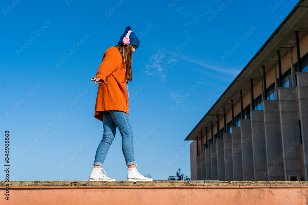 Teenage girl balancing on a wall against while listening music with headphones Teenage girl balancing on a wall against while listening music with headphones