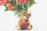 A large tulip bouquet, many flowers with red blossoms. With teddy bear.