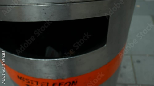 Close-up of male hand with watches throwing out empty recycling plastic bottle into public garbage bin. Recycling plastic, proper sorting of garbage.