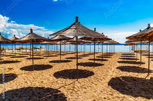 Empty beach with reed beach umbrellas  nobody on the beach. Beautiful blue sky  hot weather. Beach with no travellers and tourists. Cancellations due to coronavirus covid-19. Quarantine.