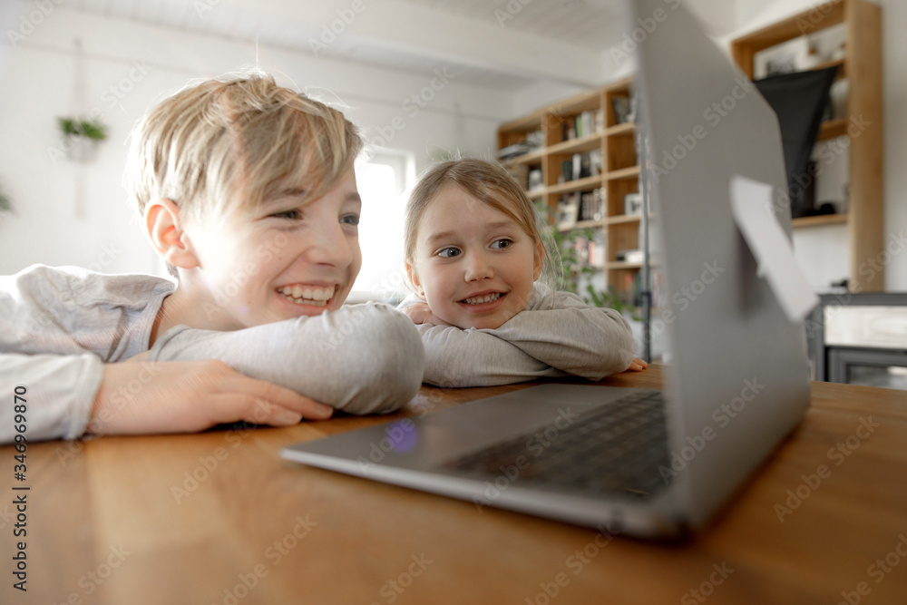 Happy brother and sister looking at laptop together at home Happy brother and sister looking at laptop together at home
