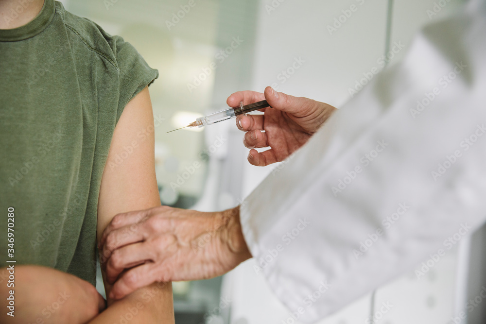 Doctor injecting vaccine into arm of teenager Doctor injecting vaccine into arm of teenager