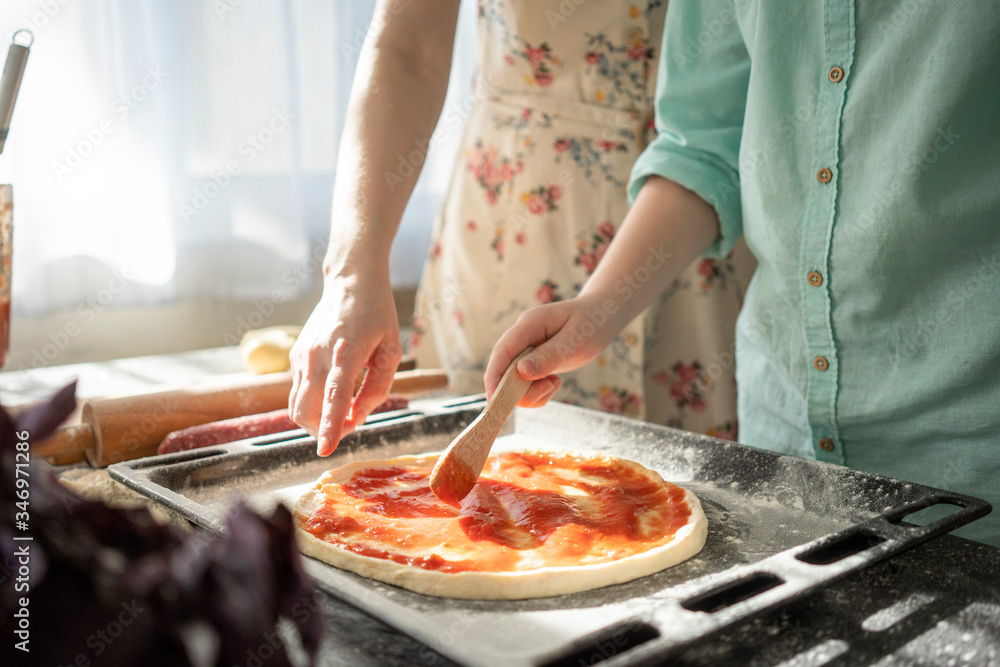 Crop view of boy spreading tomato sauce on pizzy base Crop view of boy spreading tomato sauce on pizzy base