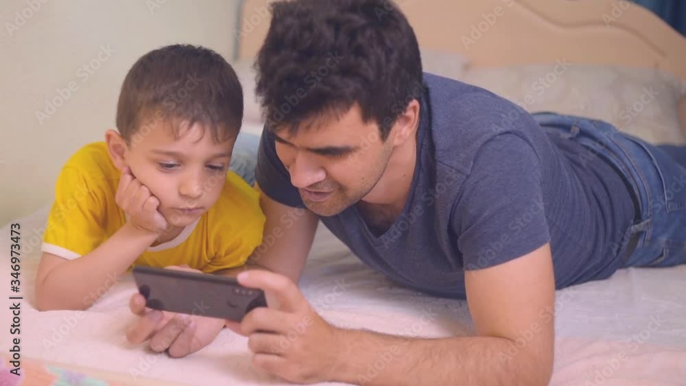 the boy and his father look at the smartphone screen, parents and children get acquainted with new technologies, the family uses gadgets to communicate the boy and his father look at the smartphone screen, parents and children get acquainted with new technologies, the family uses gadgets to communicate