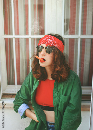 Portrait of young woman wearing headband and sunglasses smoking carrot photo