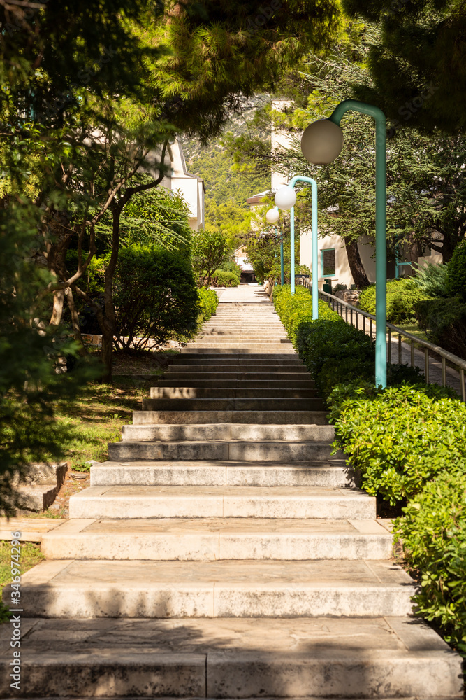 Bol, Croatia, 10th September 2019. Long stairs with trees and greenery near the boulevard on island Brac in Dalmatia. Modern lanterns next to the path. Relaxing summer feeling, holiday, vacation