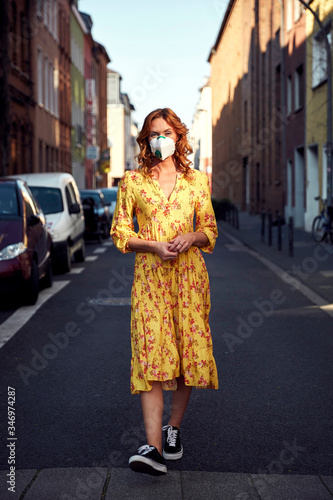 Red-haired woman wearing a FFP2 face mask and walking on empty road