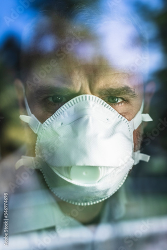 Mature man with protective mask looking through of the window, looking at camera photo