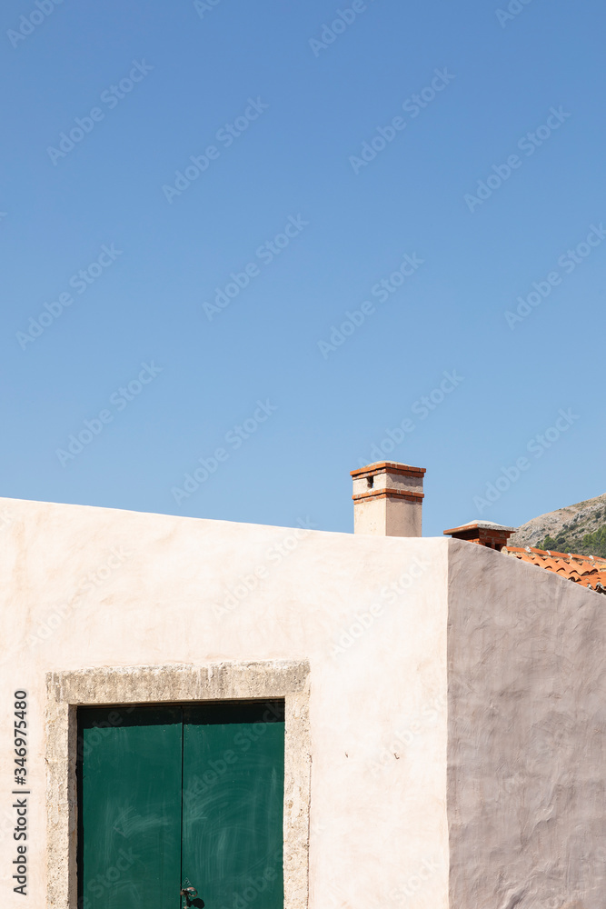 A minimalistic mediterranean house with a dark green door, bright white facade with a structure and a chimney on a sunny day in summer and a clear blue sky in Dalmatia Croatia