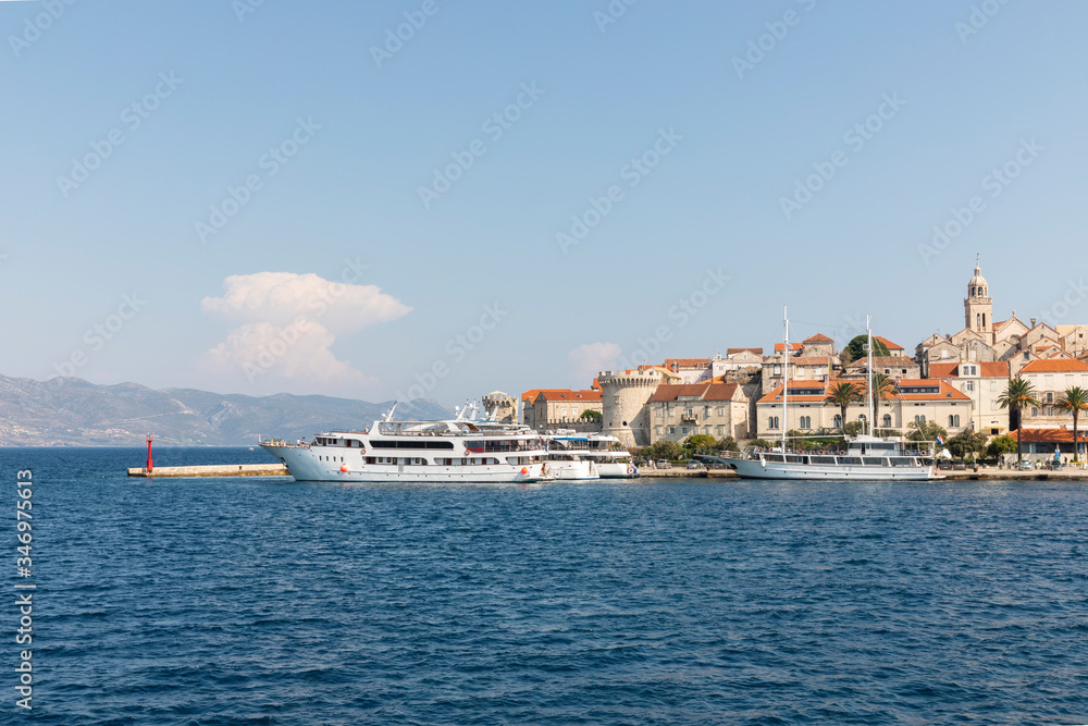 Korcula island with the old city walls, view from the sea on a sunny day in the summer blue sky. Clear adriactic sea and cruise ships docked at harbor. The south mediterranean coast of Croatia, Europe