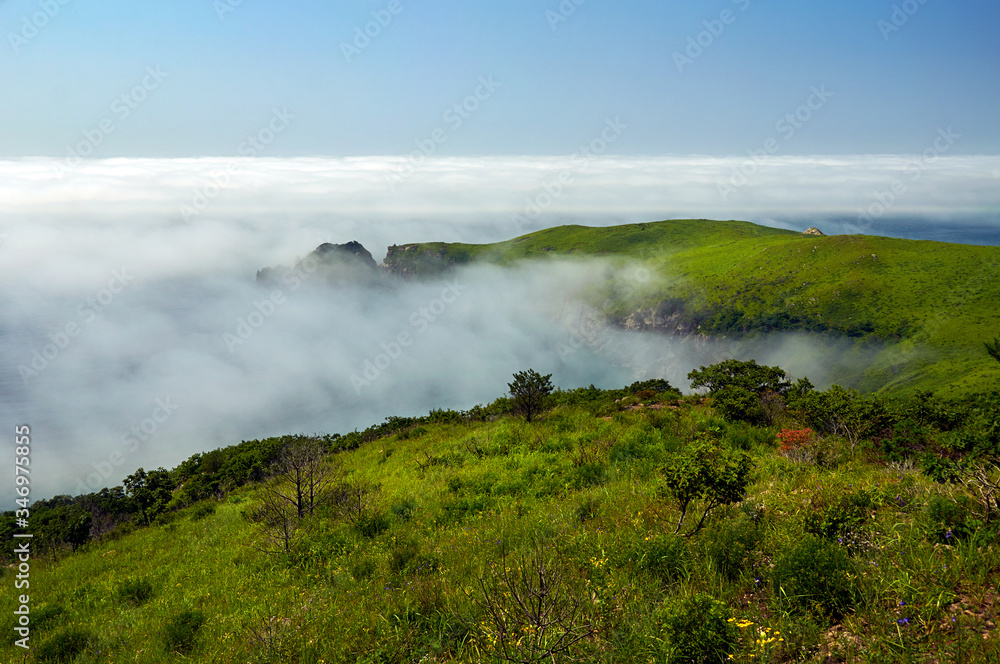 Sea lagoon in the fog surrounded by steep shores and green hills. View from above.