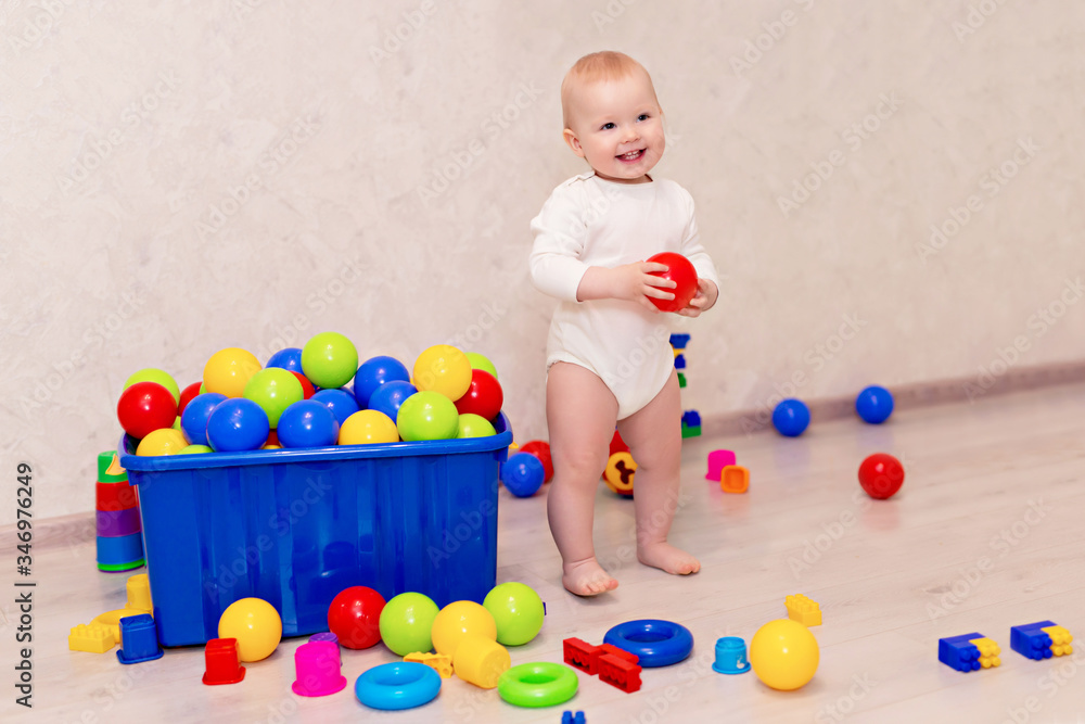 Obraz premium little baby in white clothes sits and plays with a multi-colored designer at home, child development