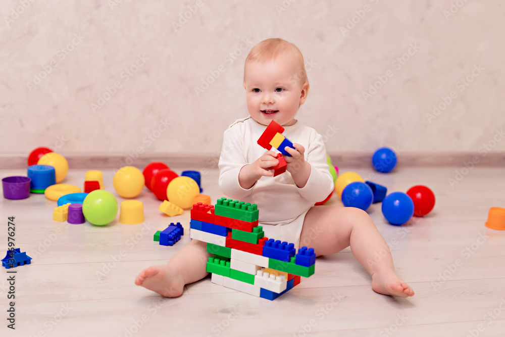 Obraz premium little baby in white clothes sits and plays with a multi-colored designer at home, child development