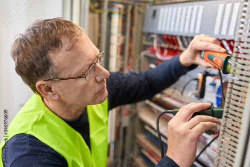 Electrician working with voltmeter at fuse box photo