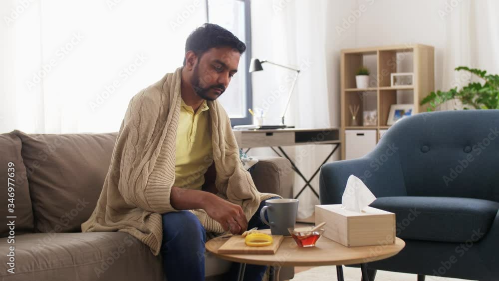 health, cold and people concept - sick young man in blanket drinking hot tea with lemon, honey and ginger at home health, cold and people concept - sick young man in blanket drinking hot tea with lemon, honey and ginger at home