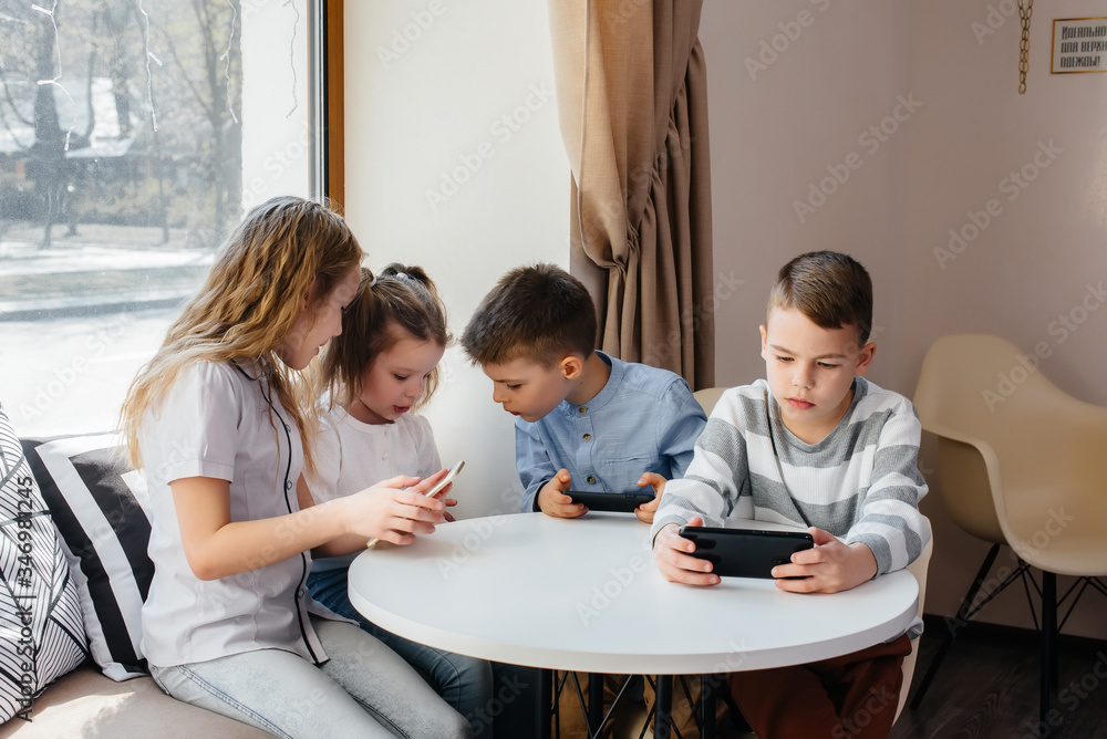 Children sit at a table in a cafe and play mobile phones together. Modern entertainment Children sit at a table in a cafe and play mobile phones together. Modern entertainment