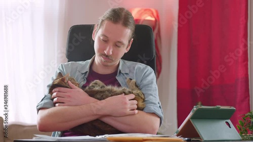 A caucasian man cuddles a cat affectionately while working from home - slow motion